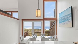 A dining area with a view of the ocean, large windows, and a hanging light fixture.