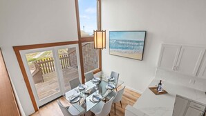 A dining area with a glass table, white chairs, and a view of the beach through a large window.