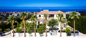 A coastal property with a central building surrounded by palm trees, a paved driveway, and a view of the sea. - Chateau Moderne Luxury Villa in Paphos with private pool and gardens (St Georges Peyia)