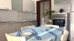 A modern kitchen with white cabinets, a built-in oven, and a dining area set with a table, chairs, and a blue tablecloth.