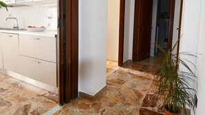 A modern kitchen with a marble floor, wooden doors, and a potted plant.