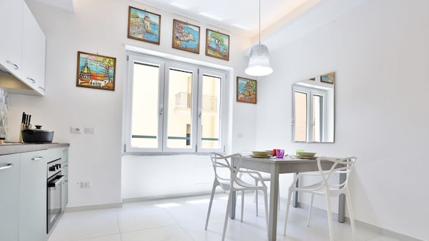 A modern kitchen with white cabinets, a dining table with chairs, and artwork on the walls. - GuestHost - Studio Apartment Gem: Compact Comfort Redefined (Salerno)
