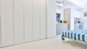 A bedroom with a bed, a wardrobe, and a kitchenette in the background. - GuestHost - Studio Apartment Gem: Compact Comfort Redefined (Salerno)