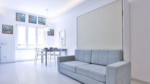 A modern living room with a grey sofa, a dining table with chairs, and artwork on the walls. - GuestHost - Studio Apartment Gem: Compact Comfort Redefined (Salerno)