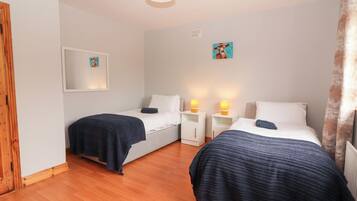 Una habitación con dos camas, cada una con una manta azul oscuro, almohadas blancas y mesitas de noche con lámparas. Hay un cuadro enmarcado en la pared y una puerta de madera a la izquierda.