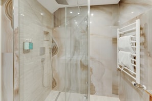 A modern bathroom with a glass-enclosed shower, marble walls, and a towel rack. - Villa Anna Kitzbühel design apartments (Kitzbuhel)