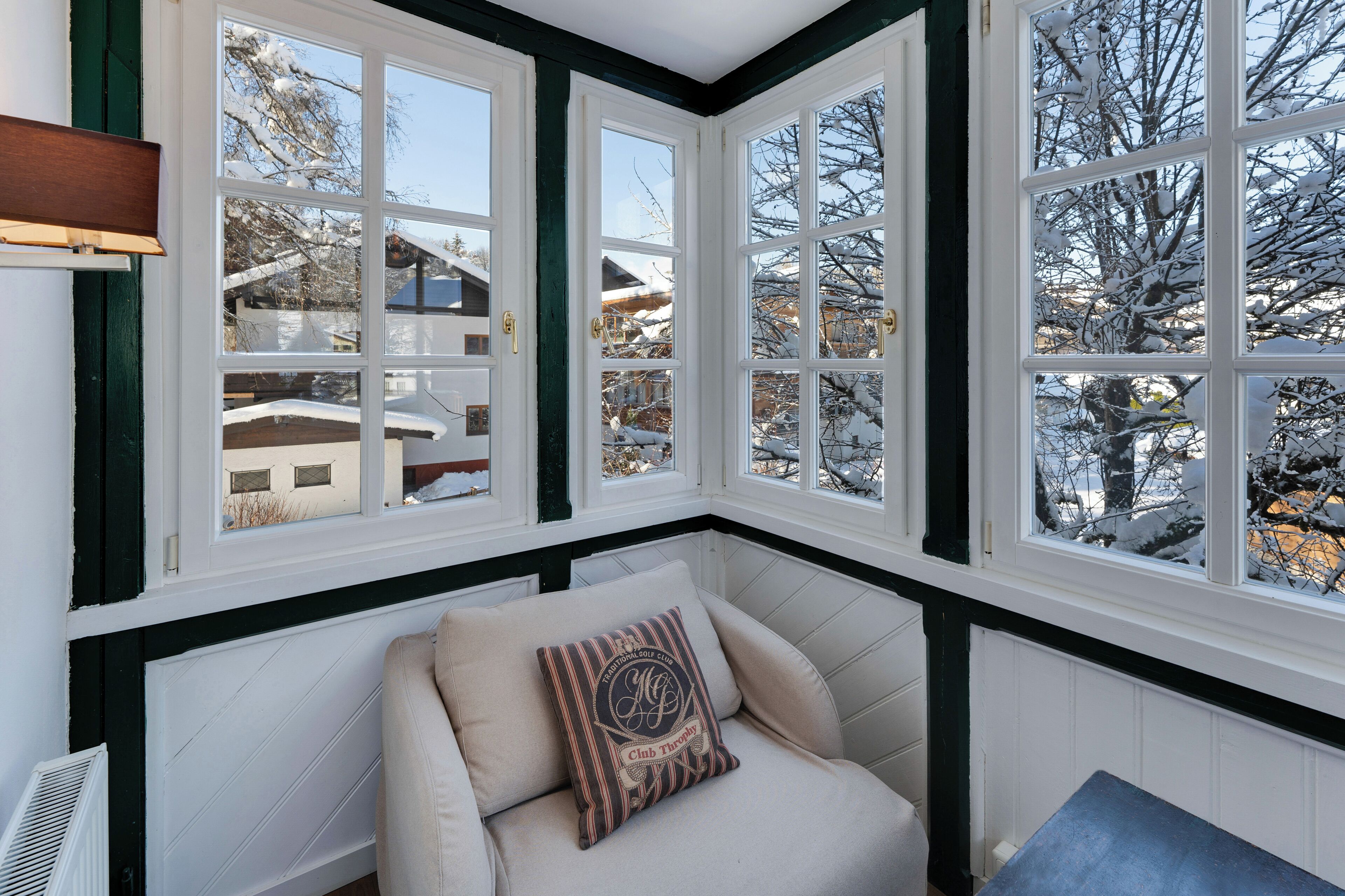 Ein Eckzimmer mit einer weißen Sitzbank, einem gemusterten Kissen und Blick auf eine verschneite Landschaft durch große Fenster.