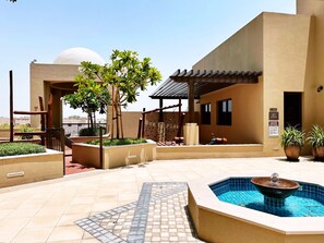 A pool area with a fountain, surrounded by potted plants and a play structure.