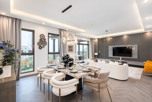 A modern living room with a large TV, a dining area with a round table and chairs, and a sofa.
