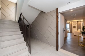 A staircase with a modern design, leading to a well-lit living area with a sofa and decorative items.