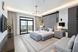 Ein modernes Schlafzimmer mit einem großen Bett, einem Nachttisch, einem Fernseher und einem Balkon mit Vorhängen.