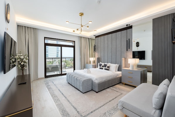 A modern bedroom with a large bed, a bedside table, a TV, and a balcony with curtains.
