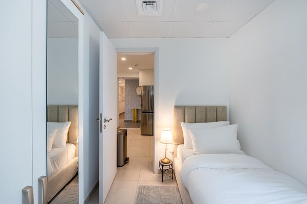 A hotel room with a bed, bedside table with a lamp, and a view into the kitchen area.