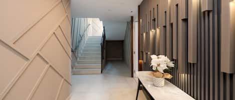 Un couloir moderne avec un banc en marbre, un escalier et un mur orné de panneaux verticaux.