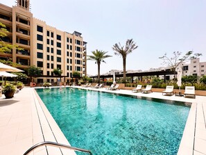 A swimming pool with lounge chairs and umbrellas, surrounded by buildings and palm trees. - Modern 4BR w/ Full Burj Al Arab View & Pvt Rooftop (Dubai)