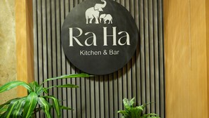 Señal para 'Ra Ha Kitchen & Bar' con un logotipo de elefantes y una planta en una maceta.