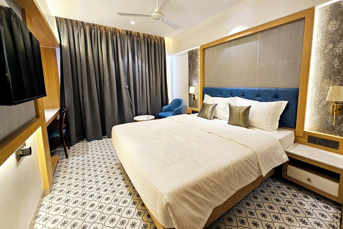 Habitación de hotel con cama, televisor, escritorio, silla, ventilador de techo y piso con diseño.