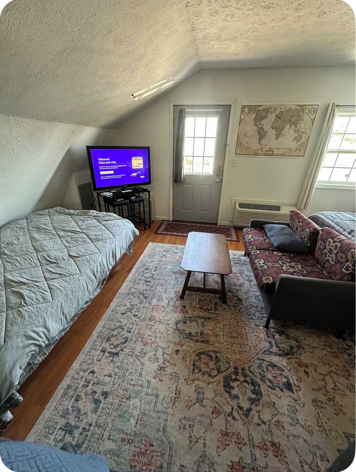 Une pièce confortable avec un lit, un canapé, une petite table, un téléviseur et une carte du monde accrochée au mur.