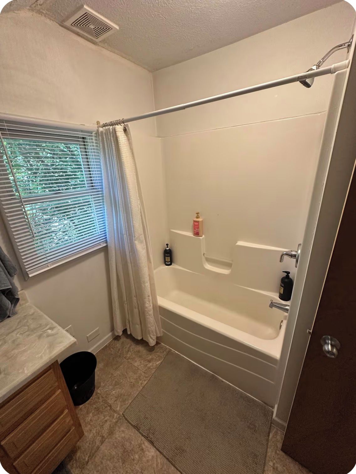 A bathroom with a bathtub, a shower curtain rod, a window with blinds, and a towel rack.