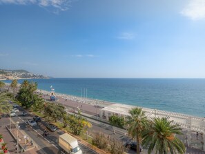 A coastal cityscape with a beach promenade, palm trees, and a clear view of the sea.