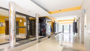 Un hall d’hôtel moderne doté d’un ascenseur en verre, d’un comptoir d’accueil et offrant une vue dégagée sur l’entrée.