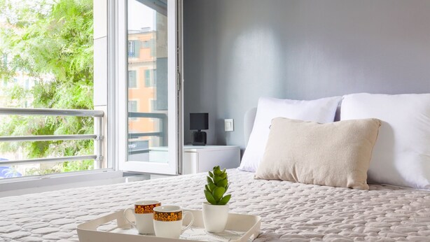 Un lit bien fait, avec un matelas matelassé, une table de chevet avec une lampe et une fenêtre donnant sur un paysage verdoyant.