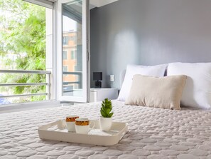 A neatly made bed with a quilted mattress, a bedside table with a lamp, and a window with a view of greenery.