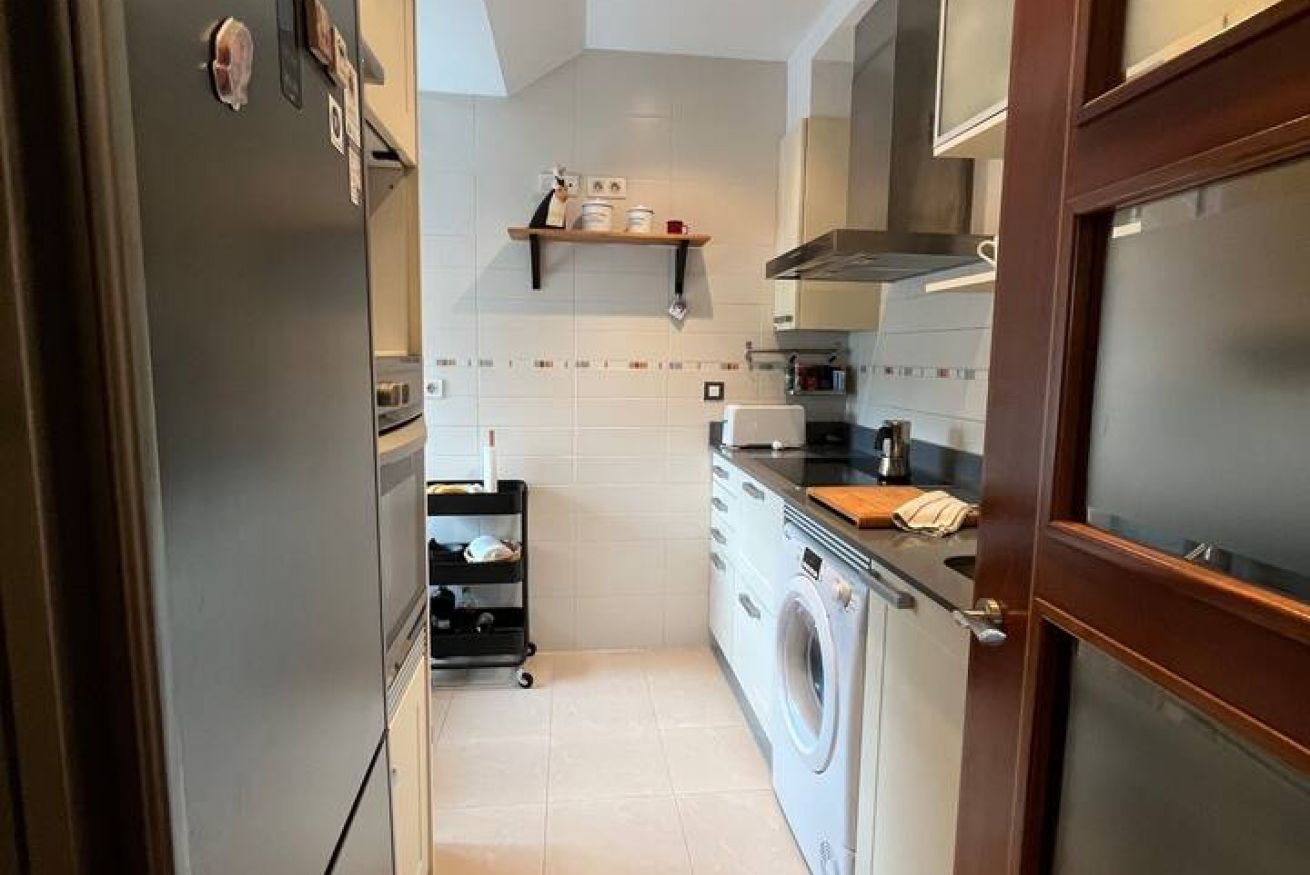 Una cocina compacta con lavadora, cafetera y repisas con utensilios de cocina.