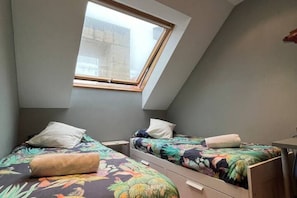 Un dormitorio con dos camas individuales, un tragaluz y un escritorio pequeño.