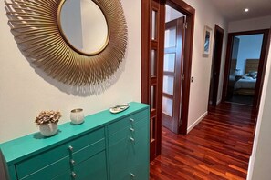 A hallway with a teal cabinet, a sunburst mirror, and wooden flooring.