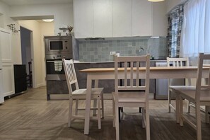 Una cuina moderna amb taula de dinar de fusta, cadires blanques i microones integrat.