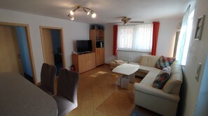 Un espace de vie compact comprenant un canapé, un téléviseur, une table à manger et un ventilateur de plafond.