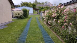 Un chemin menant à une maison dotée d’un porche abrité, entourée d’une végétation luxuriante et de plantes en fleurs.