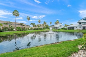 A tranquil pond with a fountain, surrounded by well-maintained grass and palm trees, with houses in the background. - Resort Style Condo, Lanai, Waterview, Pool/Tennis (Siesta Key)