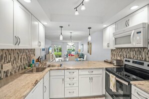 A modern kitchen with white cabinetry, a granite countertop, stainless steel appliances, and pendant lighting. - Resort Style Condo, Lanai, Waterview, Pool/Tennis (Siesta Key)