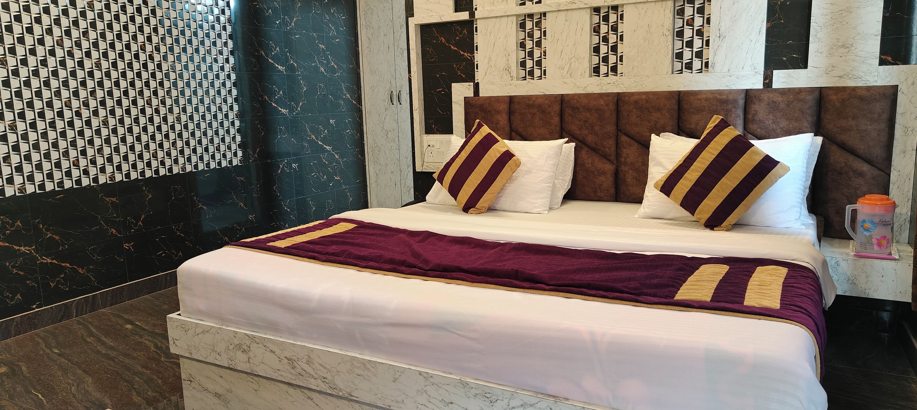 Una habitación de hotel con una cama grande, cabecera de mármol y pared con estampado.