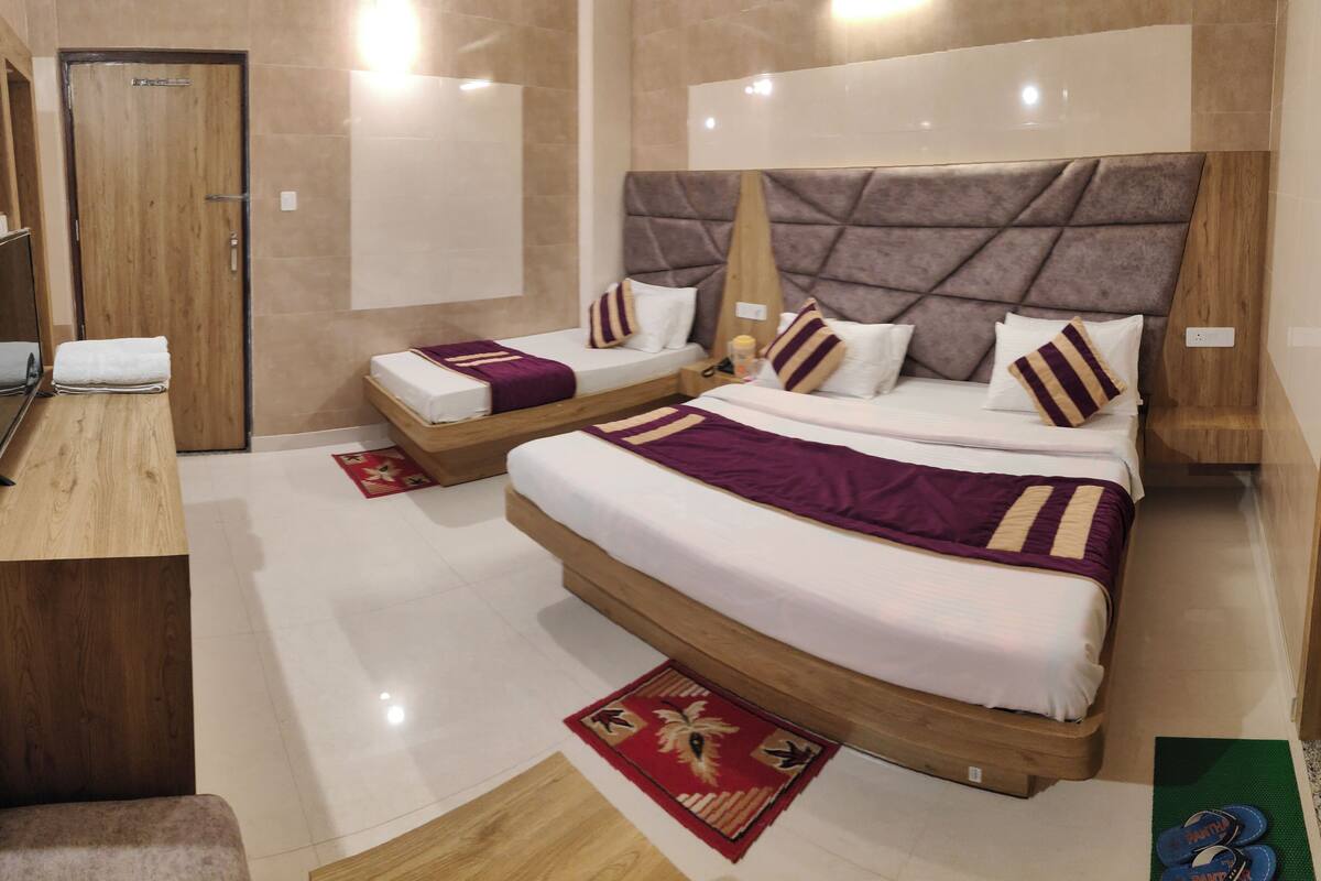 A hotel room with a large bed, a smaller bed, a wooden nightstand, a mirror, and a red and gold patterned rug.