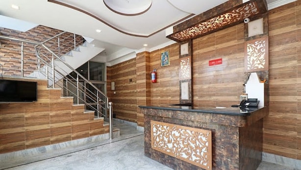 A reception area with a wooden reception desk, a staircase, and a fire extinguisher on the wall. - Hotel Sunshine (Reasi)
