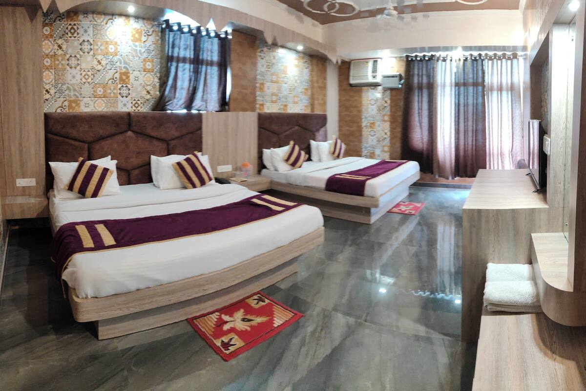 A hotel room with two beds, a wooden headboard, patterned wall tiles, a red rug, and a wooden bench.