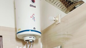 A bathroom with a white sink, a mirror, and a water heater. - Hotel Sunshine (Reasi)