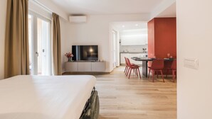 Habitación de hotel con cama, televisión, escritorio con sillas y zona de cocina.