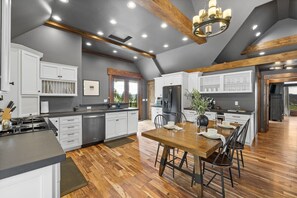 A spacious kitchen with a central island, wooden flooring, and a dining area with a table set for four. - Castle in the Sky- Overlooking Rapid City (Rapid City)