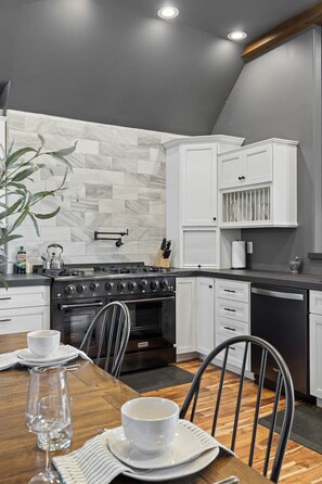 A modern kitchen with a built-in stove, white cabinetry, and a dining area with a wooden table and chairs. - Castle in the Sky- Overlooking Rapid City (Rapid City)