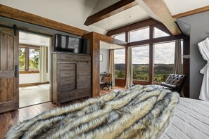 A bedroom with a large bed, a wooden dresser, a television, and a view of the outdoors.
