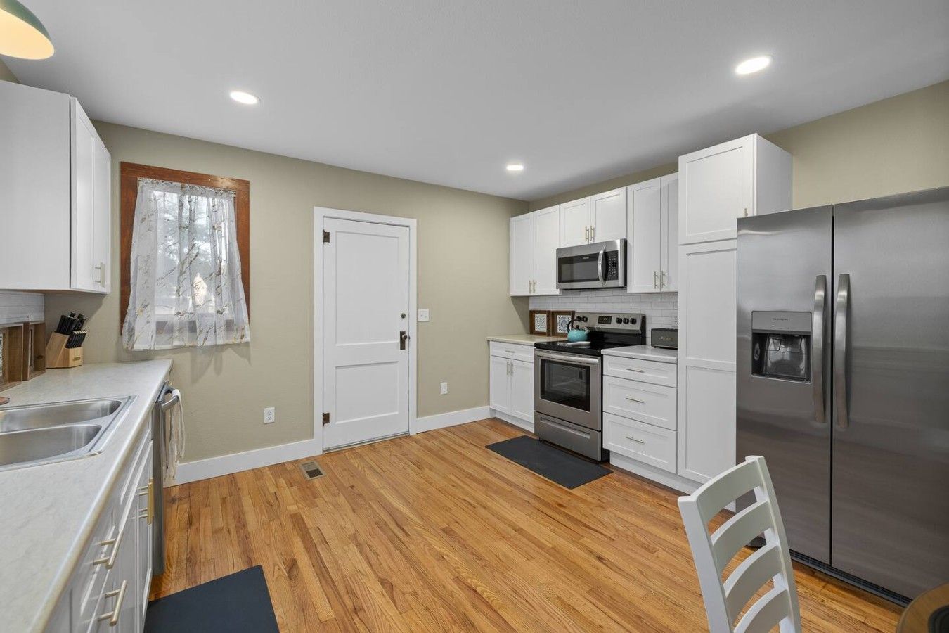 A modern kitchen with white cabinets, stainless steel appliances, and a wooden floor.