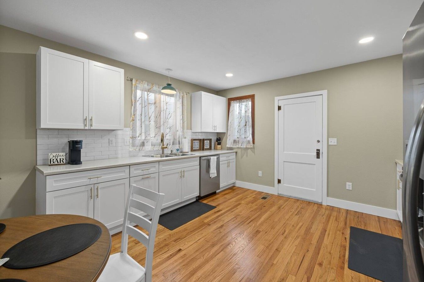 A modern kitchen with white cabinets, a coffee maker, and a wooden dining table.