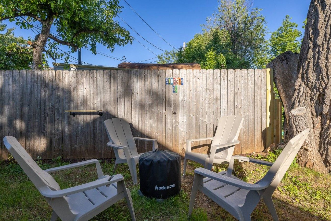 A backyard with a wooden fence, two Adirondack chairs, and a black Solo Stove backpack.