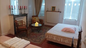 A bedroom with a bed, a chair, a table with candles, a fireplace, and a window. - The house by the water (Graçay)