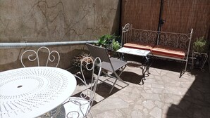 A patio with a round table and metal chairs, a bench, and potted plants. - The house by the water (Graçay)