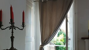 A room with a candelabra, a window with curtains, and a view of greenery outside. - The house by the water (Graçay)
